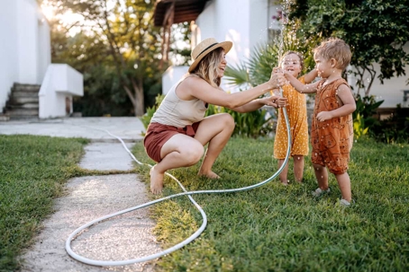 a woman and two kids playing with the water hose on the front lawn